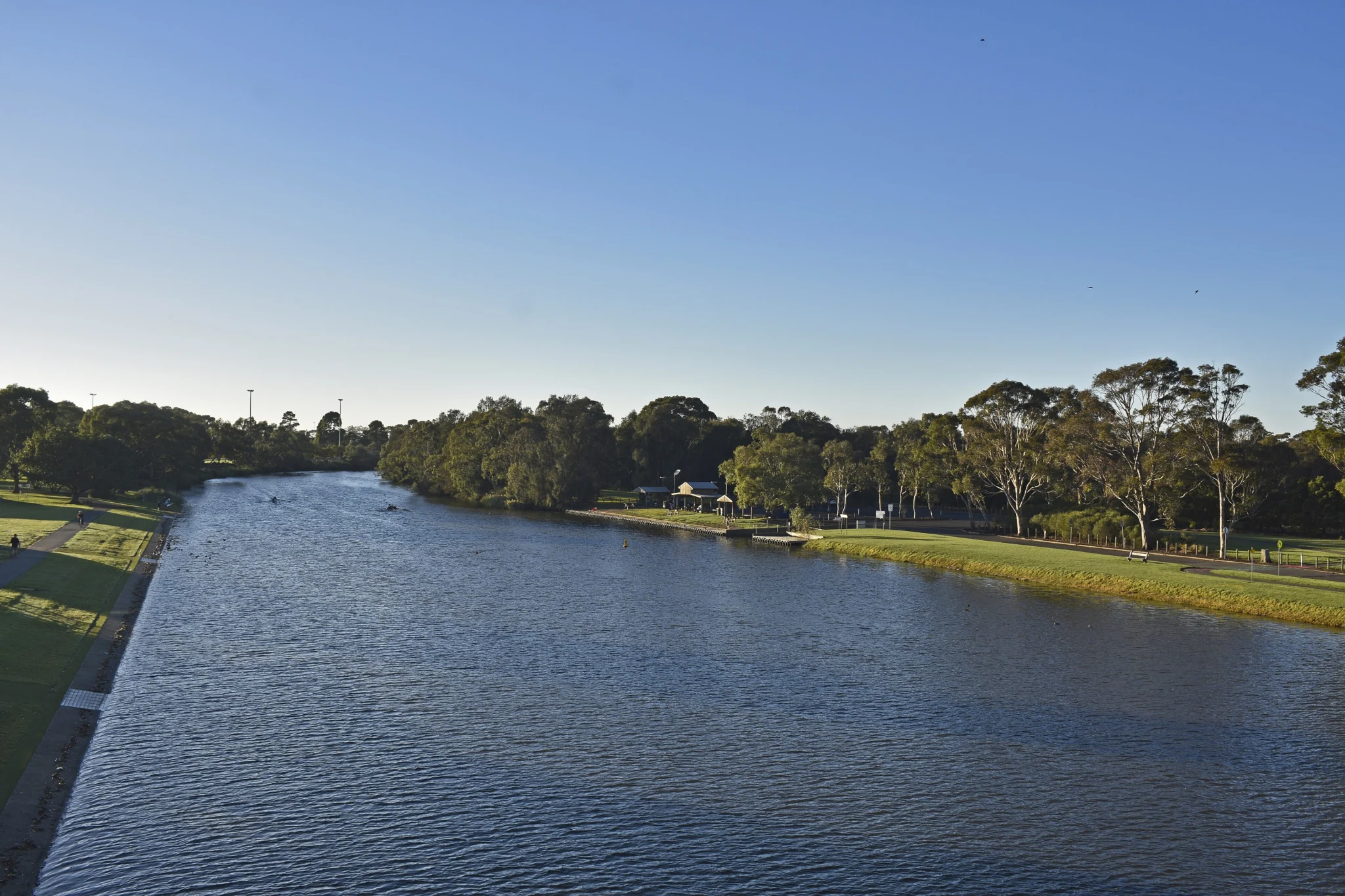 The calm Barwon River in Geelong, lined with grassy parkland and gum trees in soft afternoon light