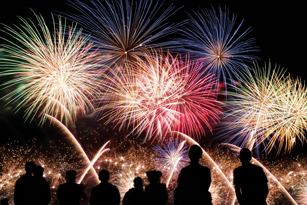 Silhouetted people watching a colourful fireworks display at night