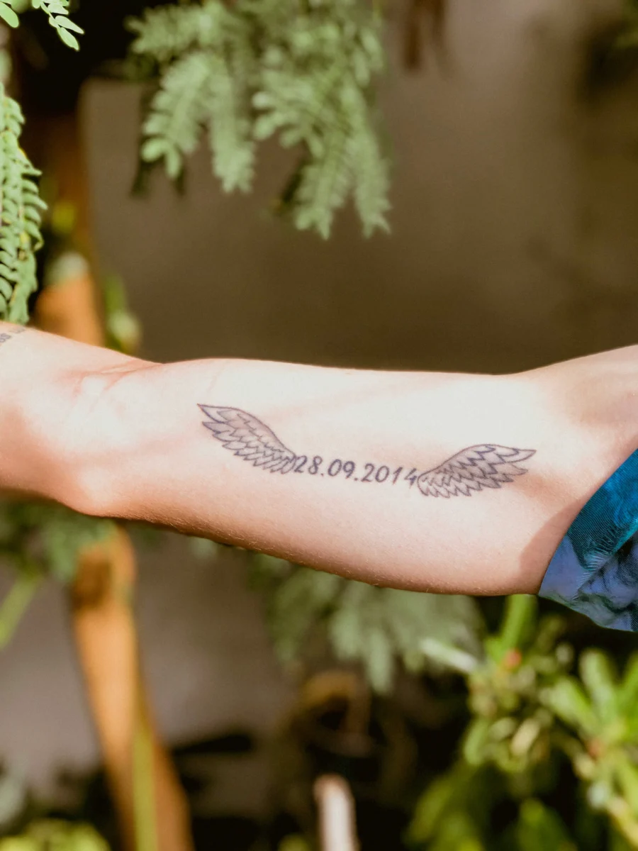 Forearm with a memorial tattoo of angel wings either side of a date