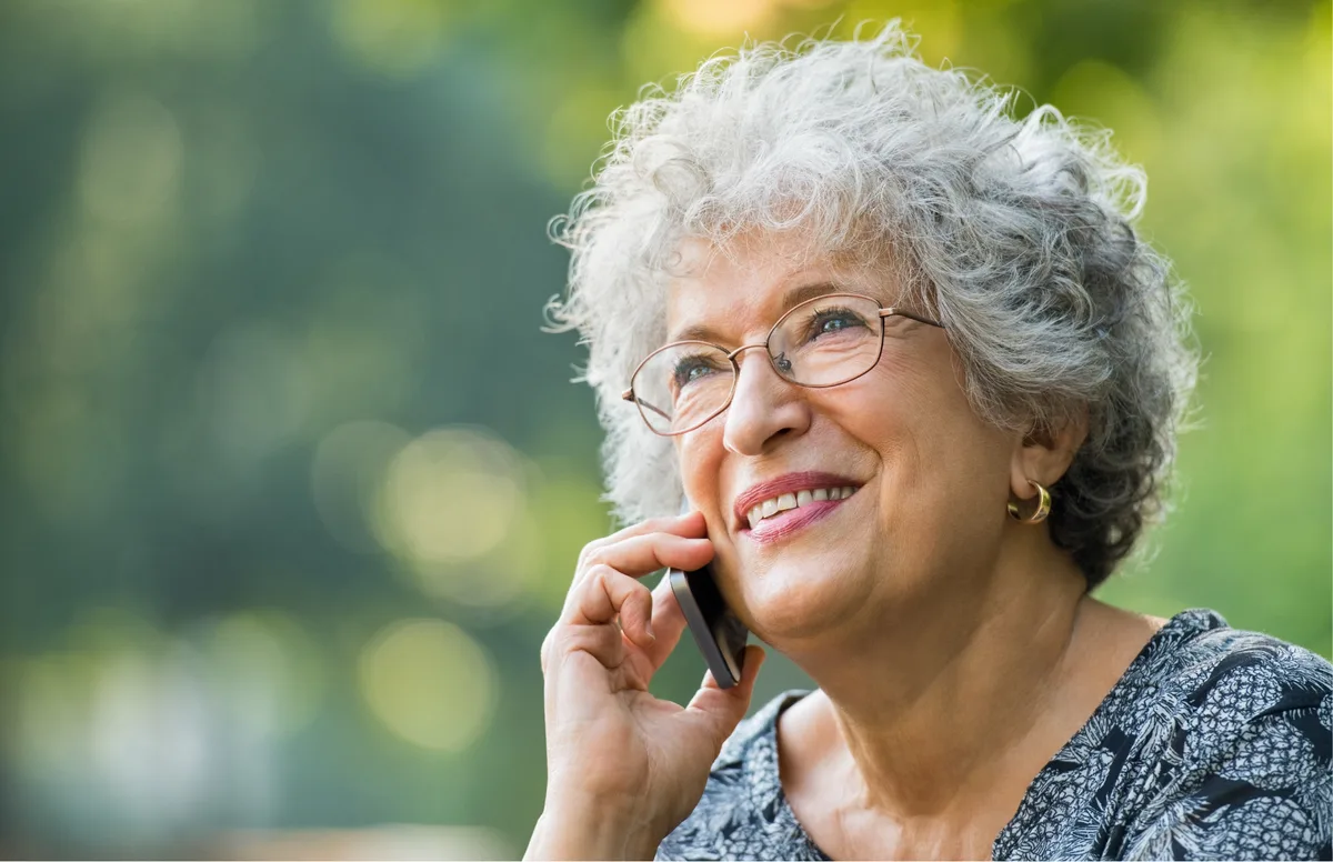Smiling older woman with grey curly hair and glasses talking on a mobile phone
